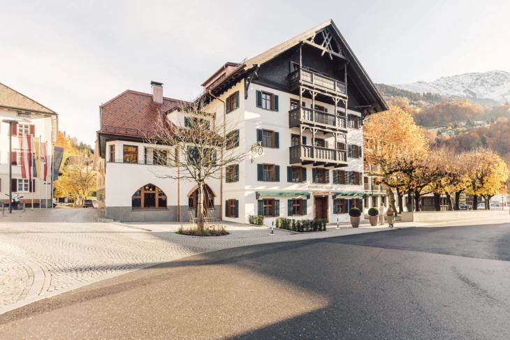 Das Posthotel Taube in Dalaas mit seinen Holzbalkonfassaden und einer Kopfsteinpflastergasse im Herbst bei sonnigem Wetter.