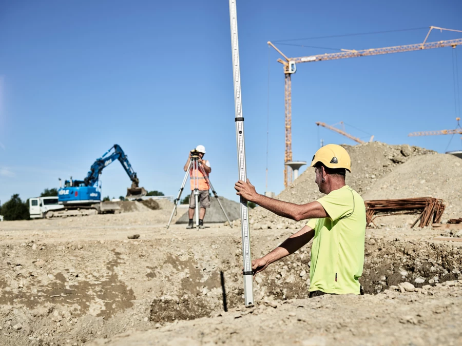 Zwei Männer auf Baustelle mit Bagger im Hintergrund Zwei Männer auf Baustelle mit Bagger im Hintergrund